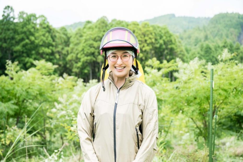 山の中で林業用ヘルメットをかぶって微笑む大村さん